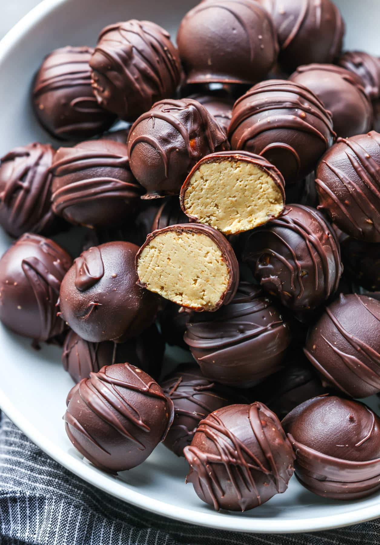 Peanut Butter balls in a white serving bowl with one cut in half showing the inside.