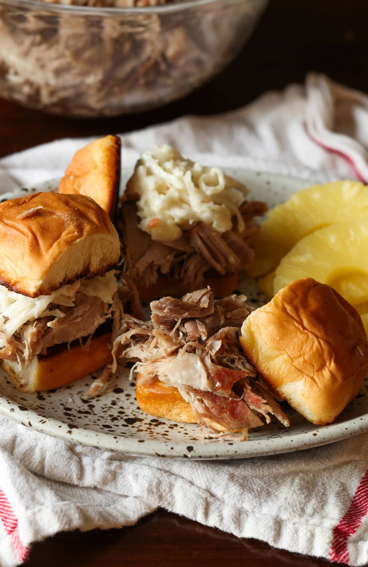 Pulled pork on a Hawaiian roll on a plate with pineapple slices
