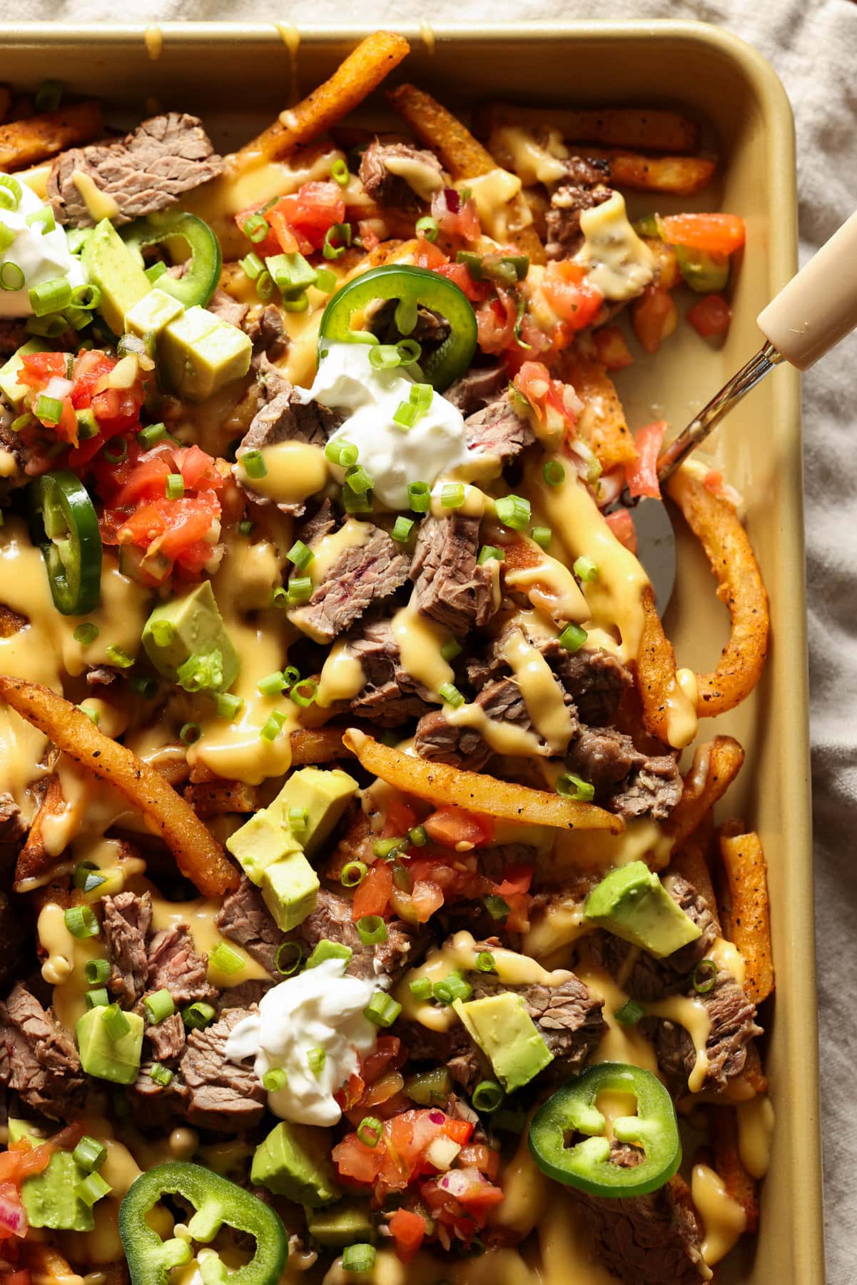 Carne Asada Fries Are a Tex Mex spin on loaded french fries. Marinated, grilled carne asada is sliced and served on top of seasoned fries with a cheesy sauce and all the toppings of your choice! Carne Asada topped french fries with melted cheese and all the nacho toppings.