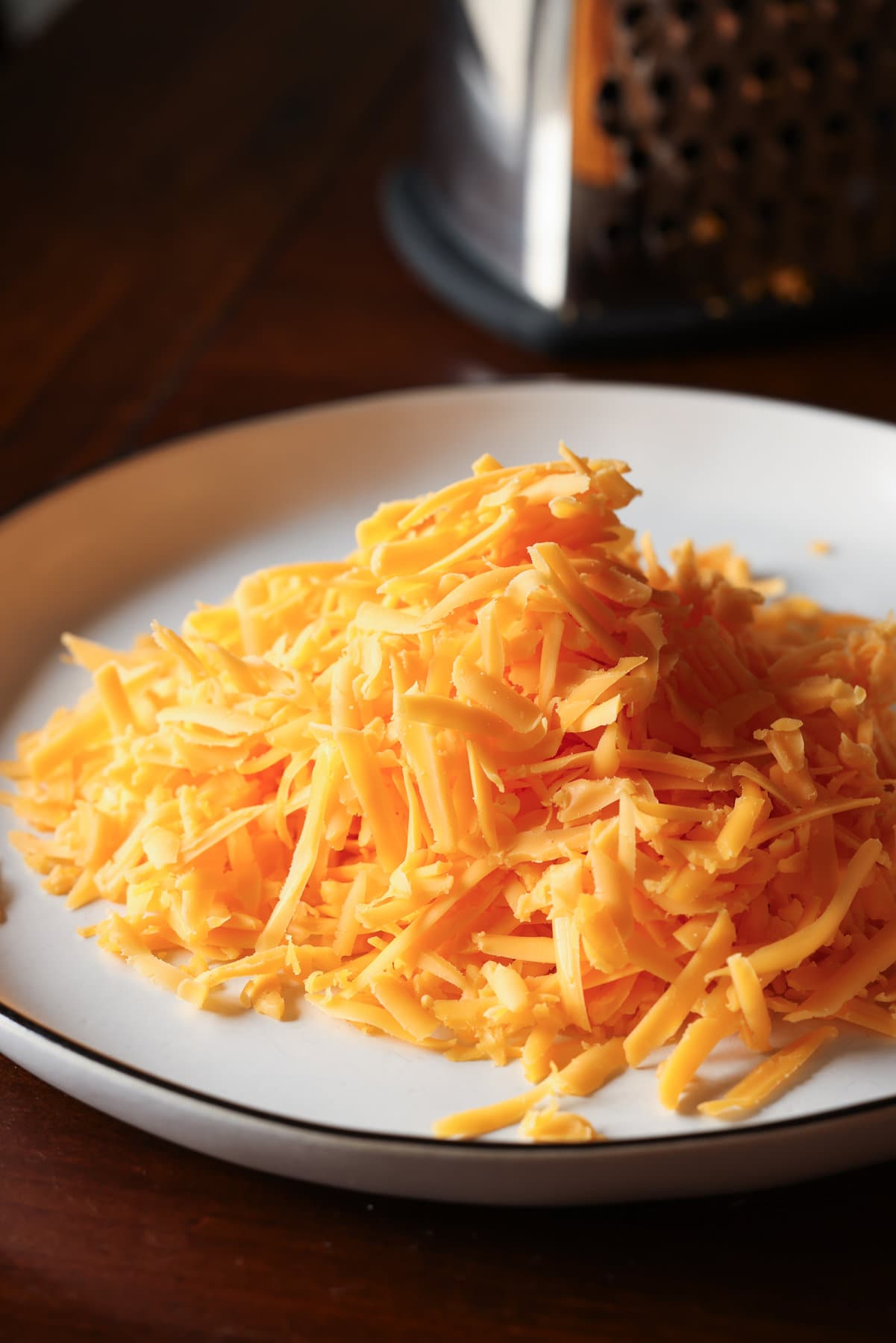 Carne Asada Fries Are a Tex Mex spin on loaded french fries. Marinated, grilled carne asada is sliced and served on top of seasoned fries with a cheesy sauce and all the toppings of your choice! Grated cheddar cheese on a white plate