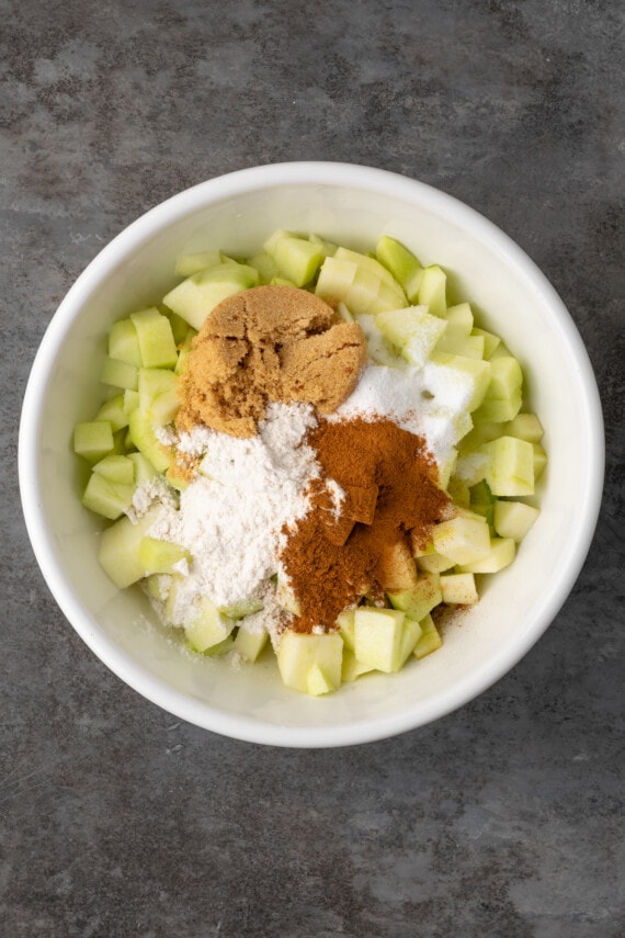 Mini apple pies are a bite-sized spin on a classic fall dessert! So easy to make and bursting with juicy apple pie filling and warm spices. Apple pie filling ingredients added to a bowl of chopped apples.