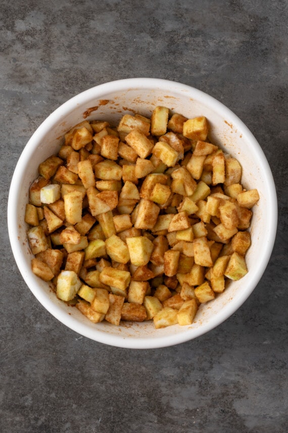 Mini apple pies are a bite-sized spin on a classic fall dessert! So easy to make and bursting with juicy apple pie filling and warm spices. Chopped apples coated in sugar and spices in a large bowl.