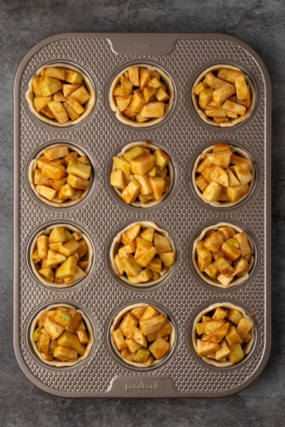 Mini apple pies are a bite-sized spin on a classic fall dessert! So easy to make and bursting with juicy apple pie filling and warm spices. Mini pie crusts filled with apple pie filling inside a 12-well muffin tin.
