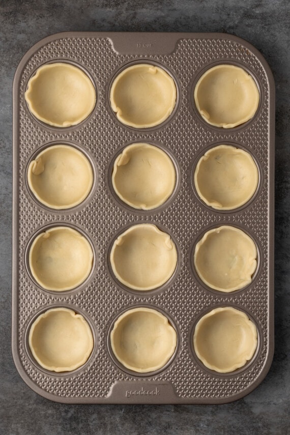 Mini apple pies are a bite-sized spin on a classic fall dessert! So easy to make and bursting with juicy apple pie filling and warm spices. Pie crust pressed into the wells of a 12-well muffin tin.
