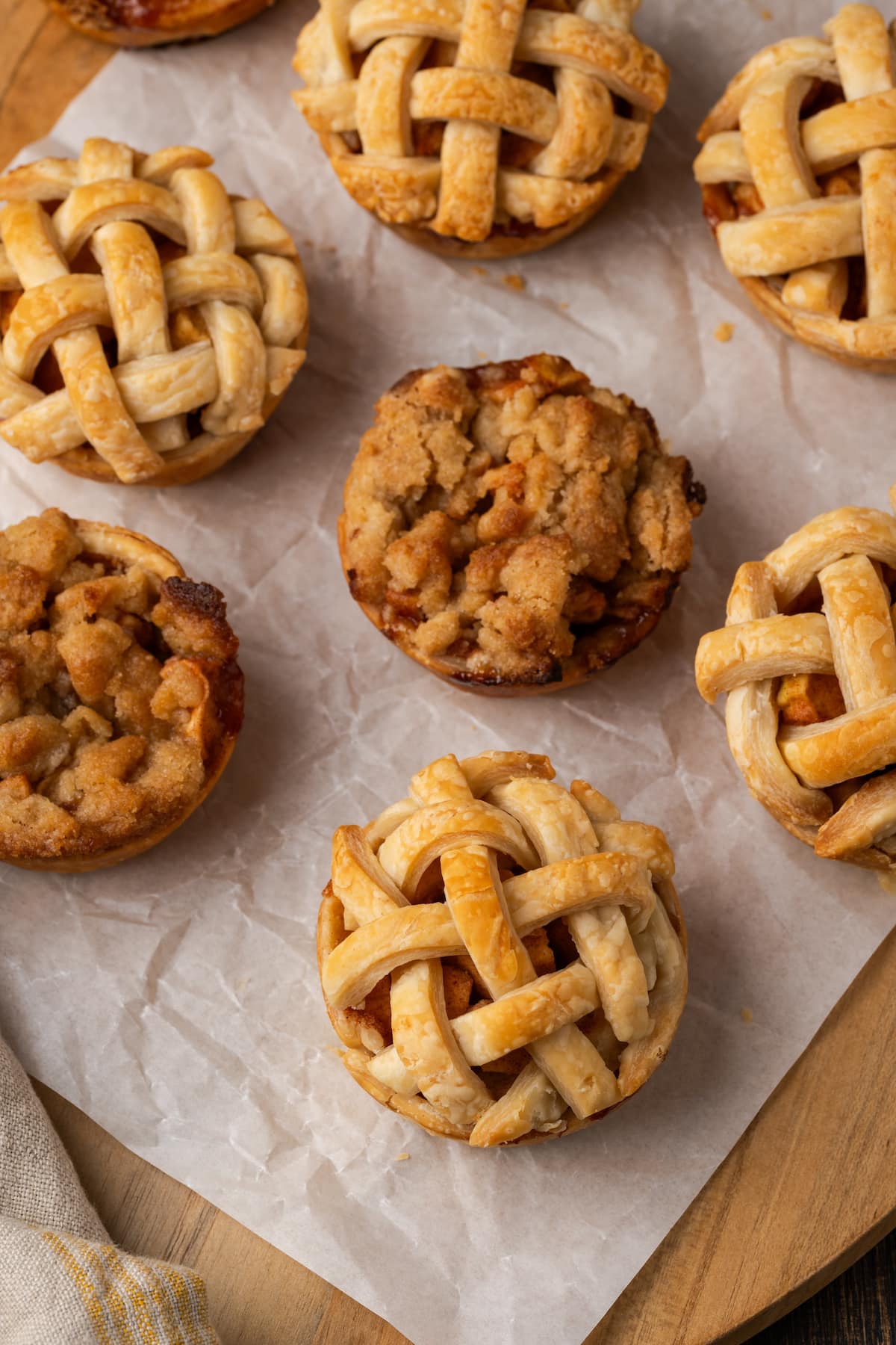 Mini apple pies are a bite-sized spin on a classic fall dessert! So easy to make and bursting with juicy apple pie filling and warm spices. Overhead view of baked mini apple pies on a piece of parchment paper.