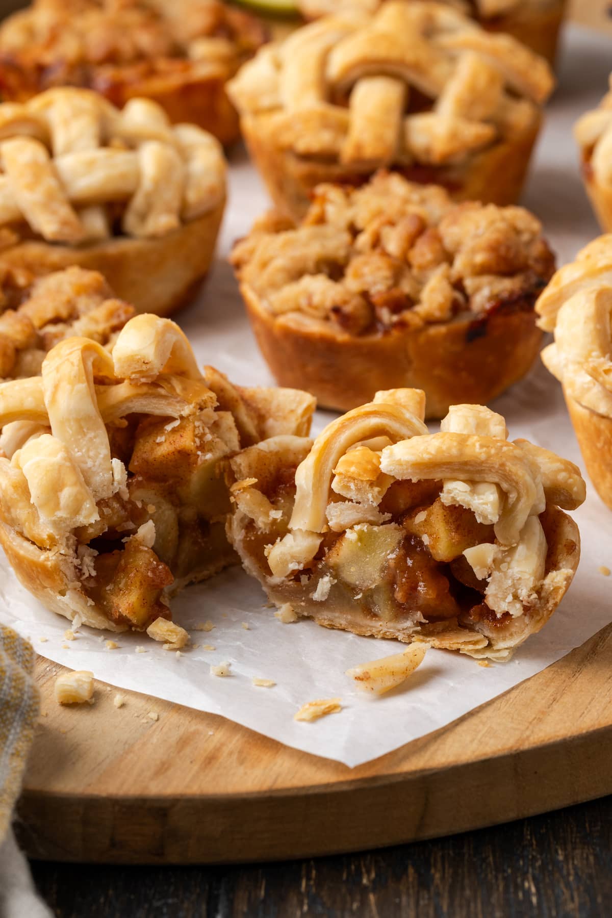 Mini apple pies are a bite-sized spin on a classic fall dessert! So easy to make and bursting with juicy apple pie filling and warm spices. Mini apple pies on a piece of parchment paper, with one pie cut in half to reveal the apple pie filling.