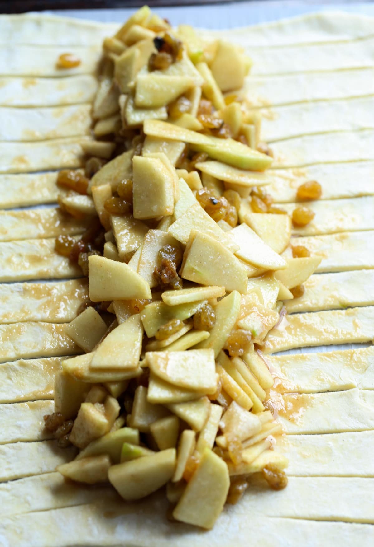 This easy Apple Strudel is filled with cinnamon, brown sugar, raisins and more! It's a crispy, flaky pastry that's easy to make and downright delicious. Chopped apples on pastry dough with the edges sliced prepping an apple strudel.