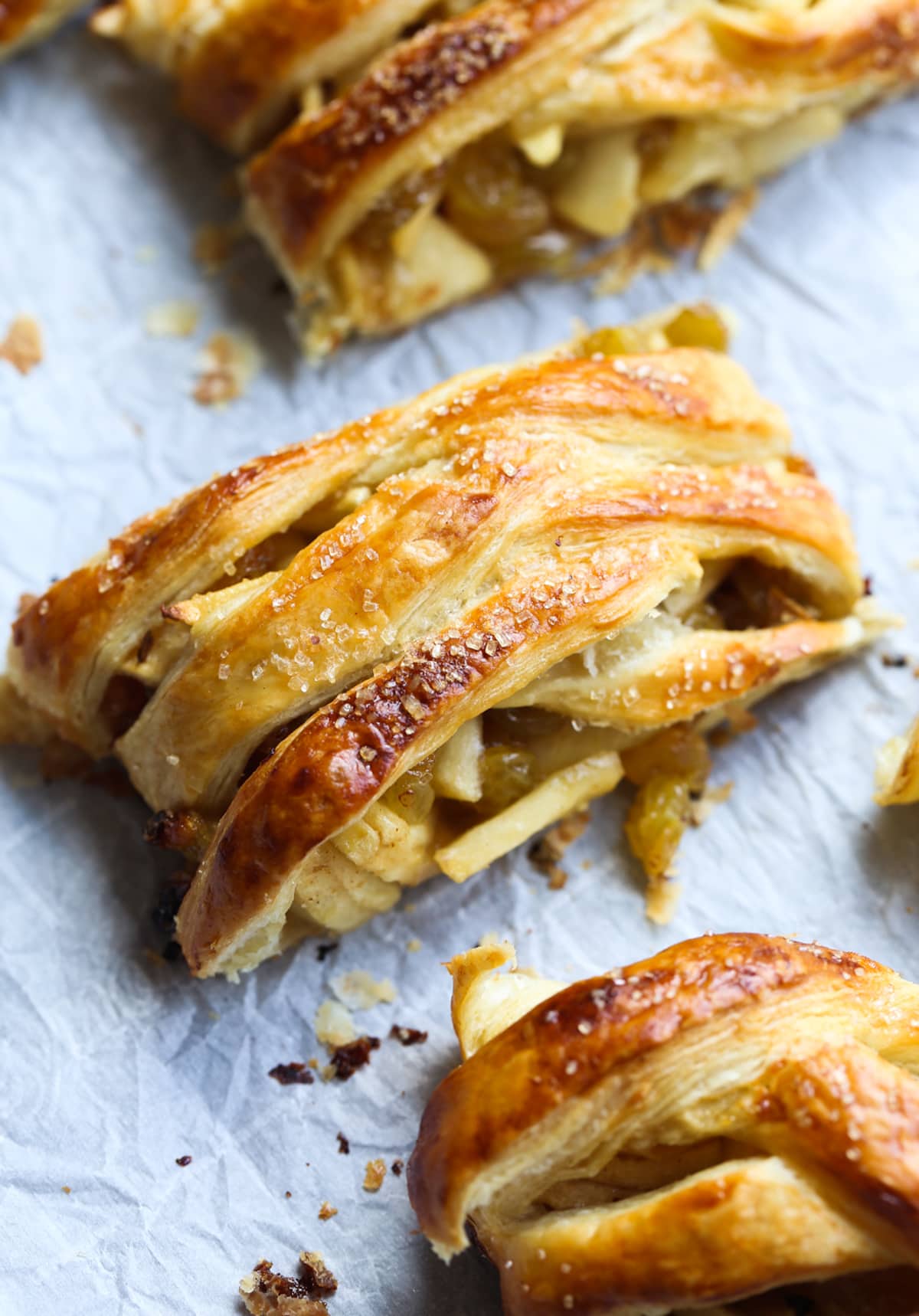 This easy Apple Strudel is filled with cinnamon, brown sugar, raisins and more! It's a crispy, flaky pastry that's easy to make and downright delicious. A slice of baked apple strudel topped with coarse sugar on a baking sheet