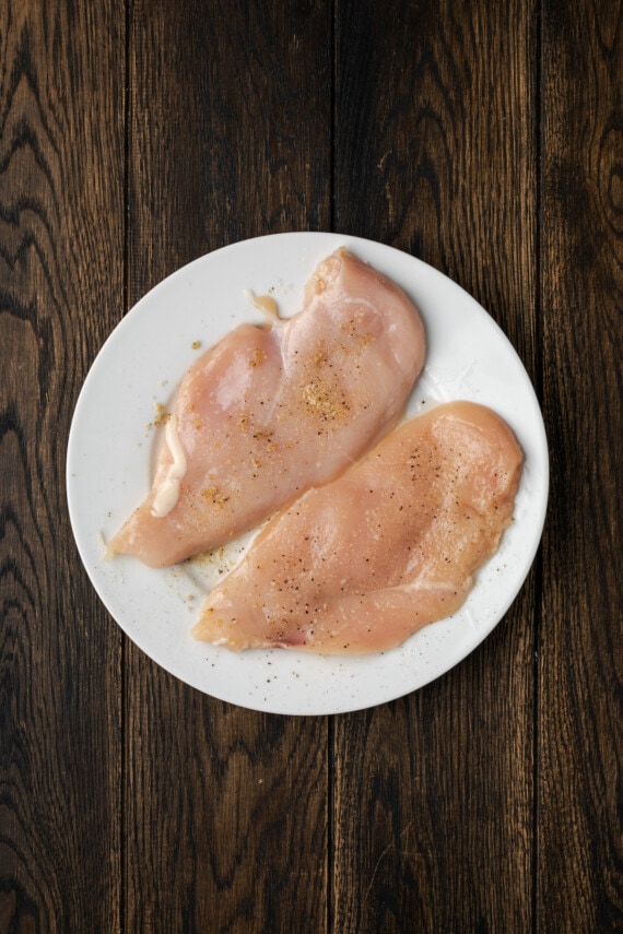 Creamy Buffalo Wild Wings Garlic Parmesan Chicken Pasta is a quick and easy dinner idea packed with bold flavor. Made with only 6 ingredients! Two uncooked, seasoned chicken breasts on a white plate.
