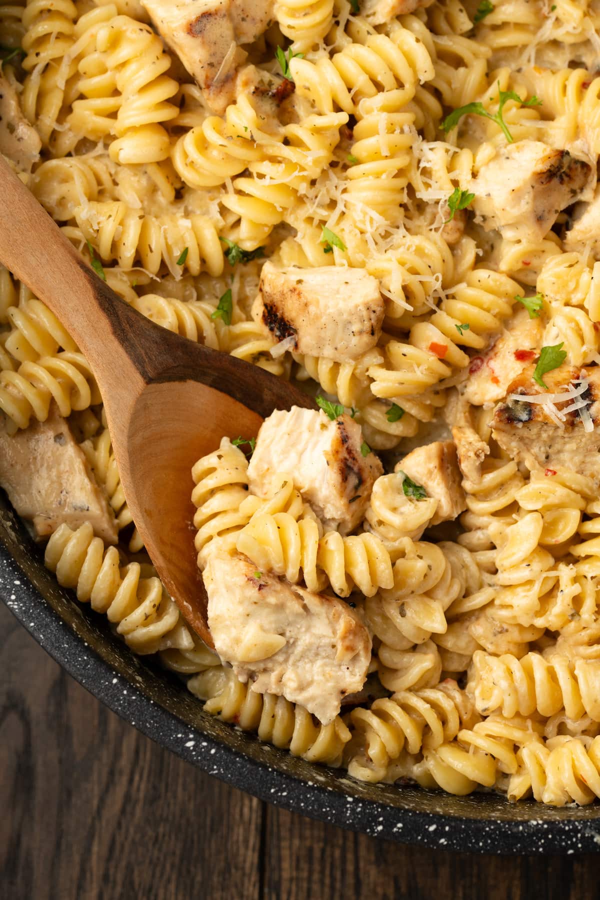 Creamy Buffalo Wild Wings Garlic Parmesan Chicken Pasta is a quick and easy dinner idea packed with bold flavor. Made with only 6 ingredients! Close up of Buffalo Wild Wings garlic parmesan chicken pasta in a skillet with a wooden spoon.