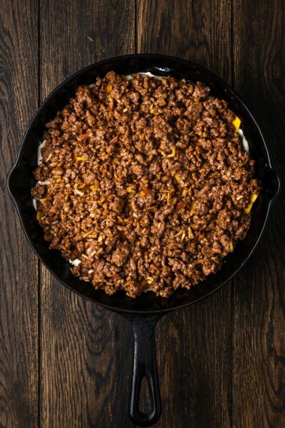 More ground beef added over top of the cheese layer in a skillet.