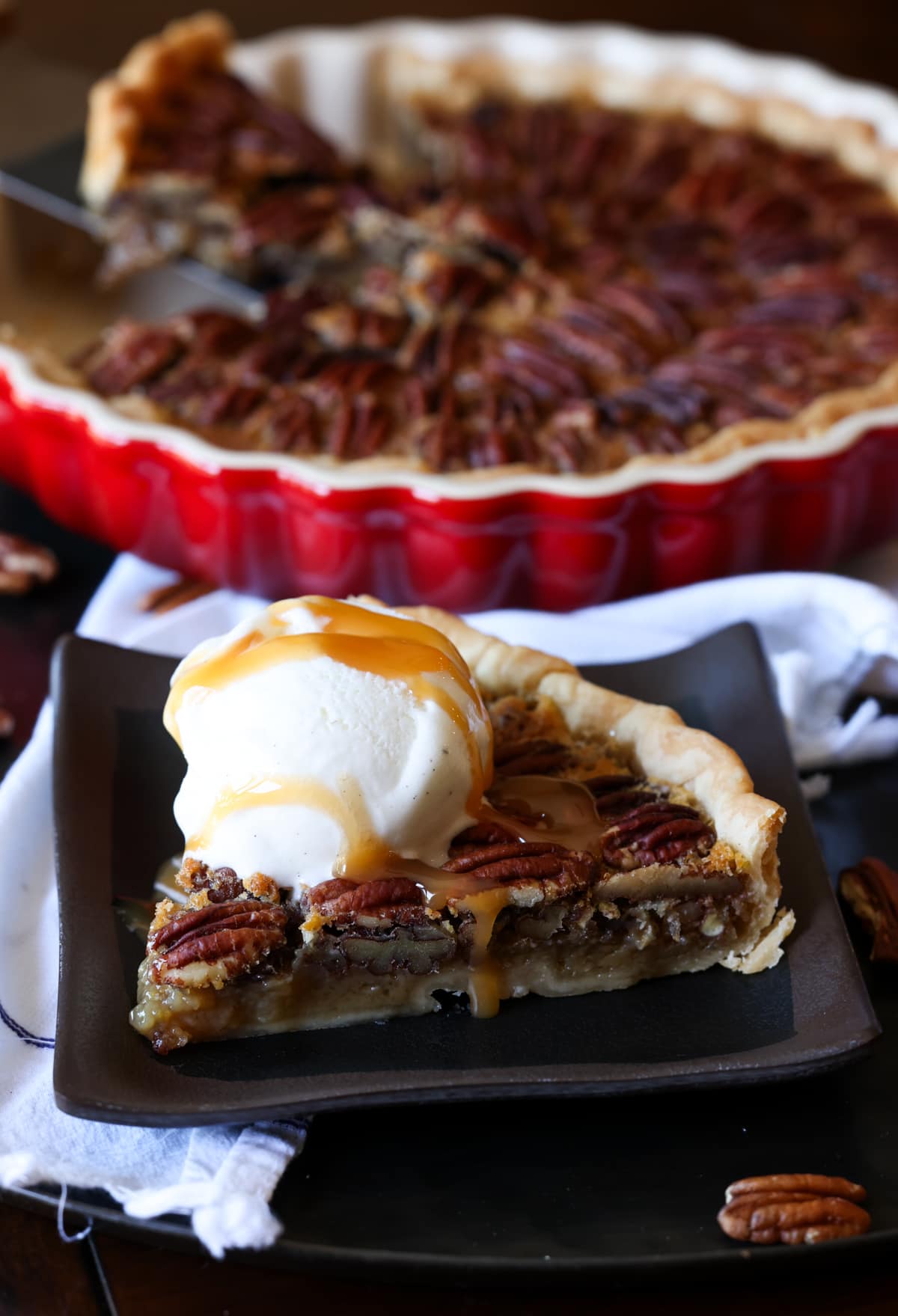 A slice of maple pecan tart on a plate with ice cream and caramel sauce