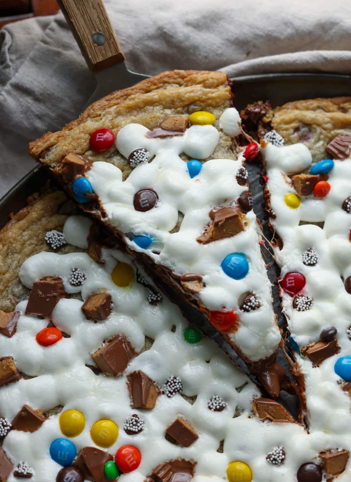 A slice of chocolate chip cookie pizza topped with melted marshmallows, M&Ms, and chopped peanut butter cups