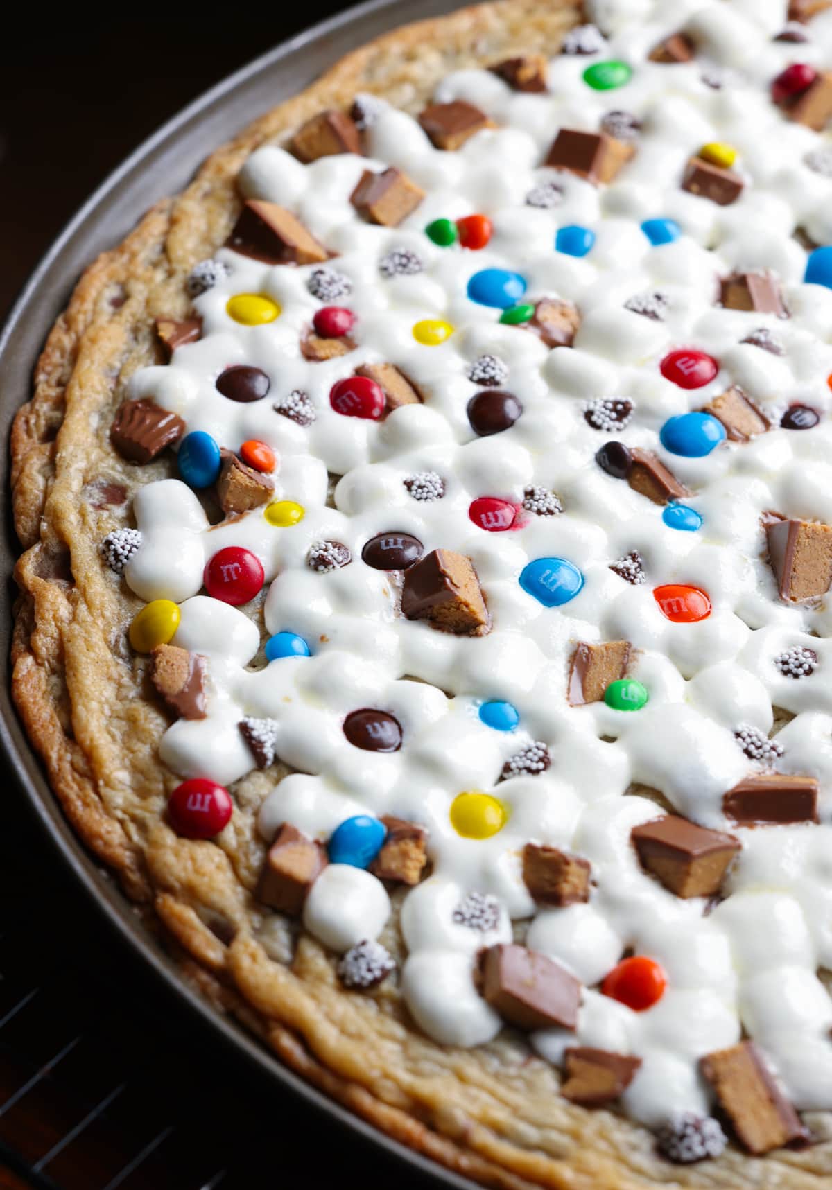 A giant chocolate chip cookie baked in a pizza pan topped with gooey melted marshmallows