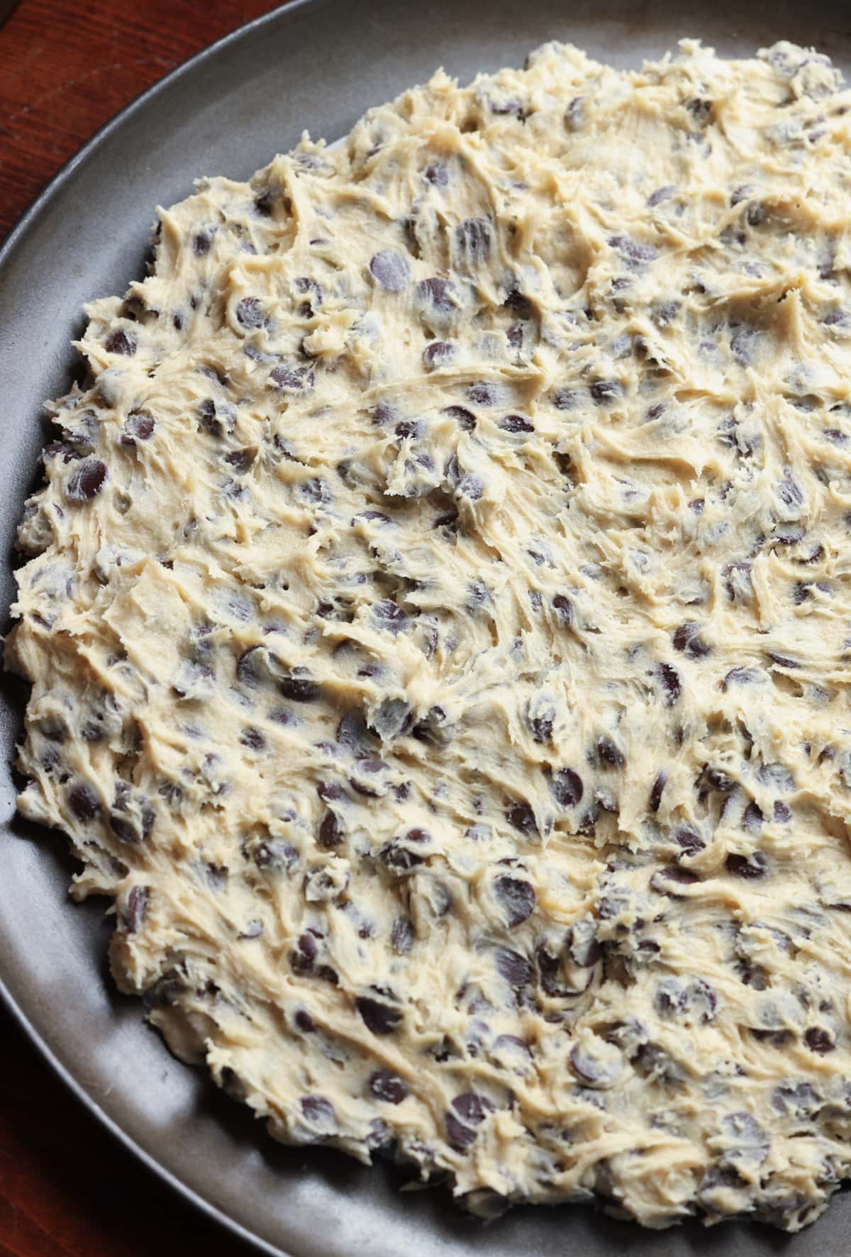 Chocolate chip cookie dough pressed into a nonstick round pizza pan before going in the oven.