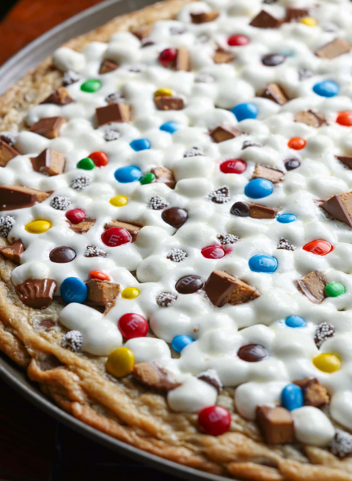 A close up of a large cookie pizza topped with chocolate candy and marshmallows