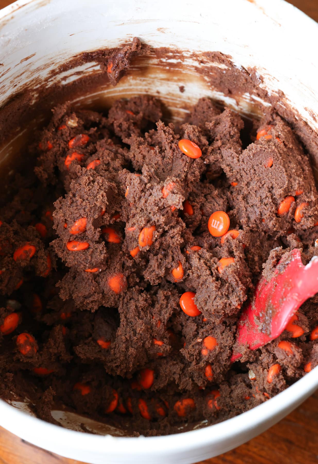 This dark chocolate cookies recipe combines the richness of dark chocolate with texture that is brownie-like, filled with chocolate candy! chocolate cookie dough in a mixing bowl with orange M&Ms