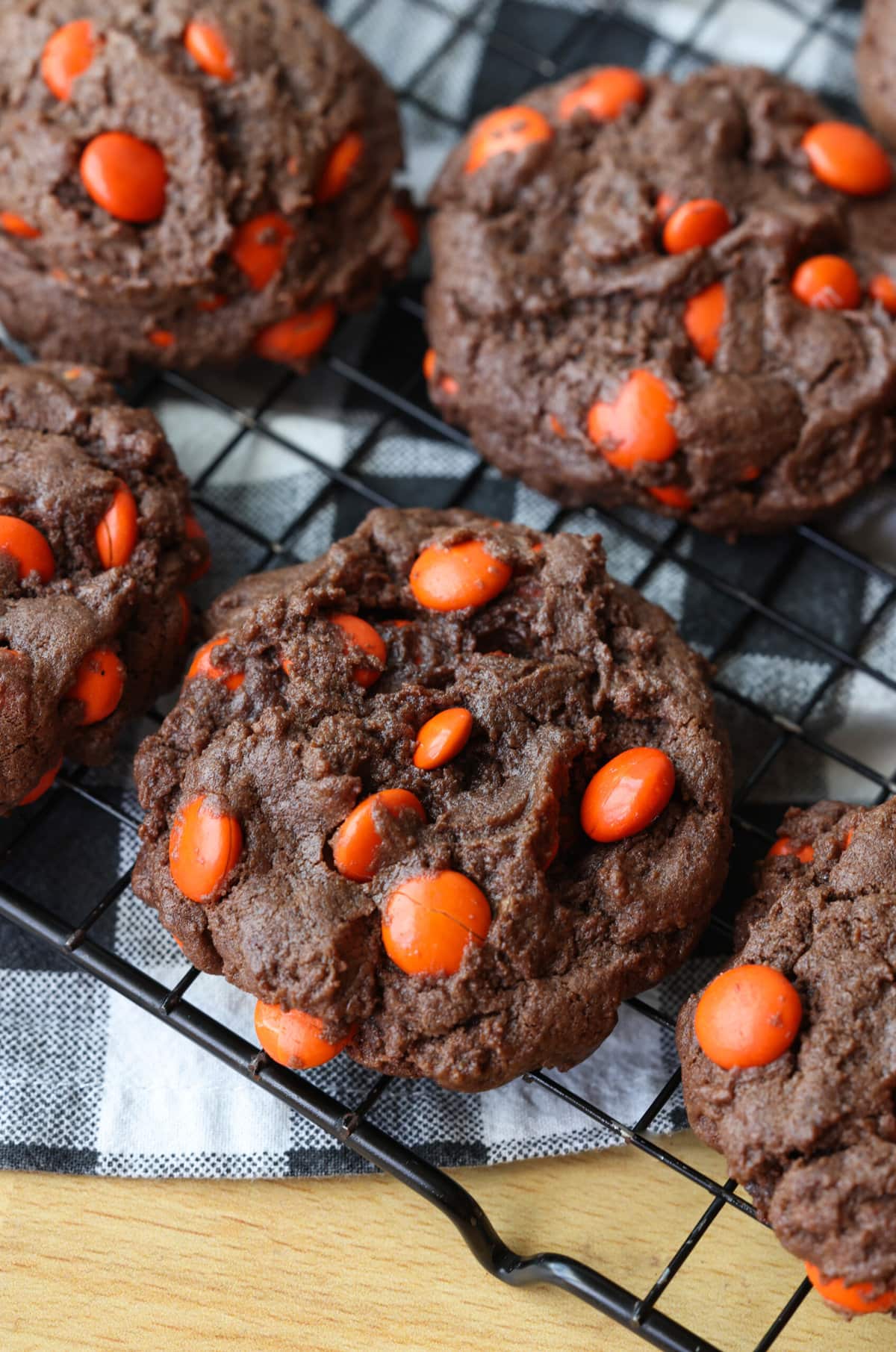 This dark chocolate cookies recipe combines the richness of dark chocolate with texture that is brownie-like, filled with chocolate candy! Dark Chocolate Cookies with orange M&Ms on a wire cooking rack