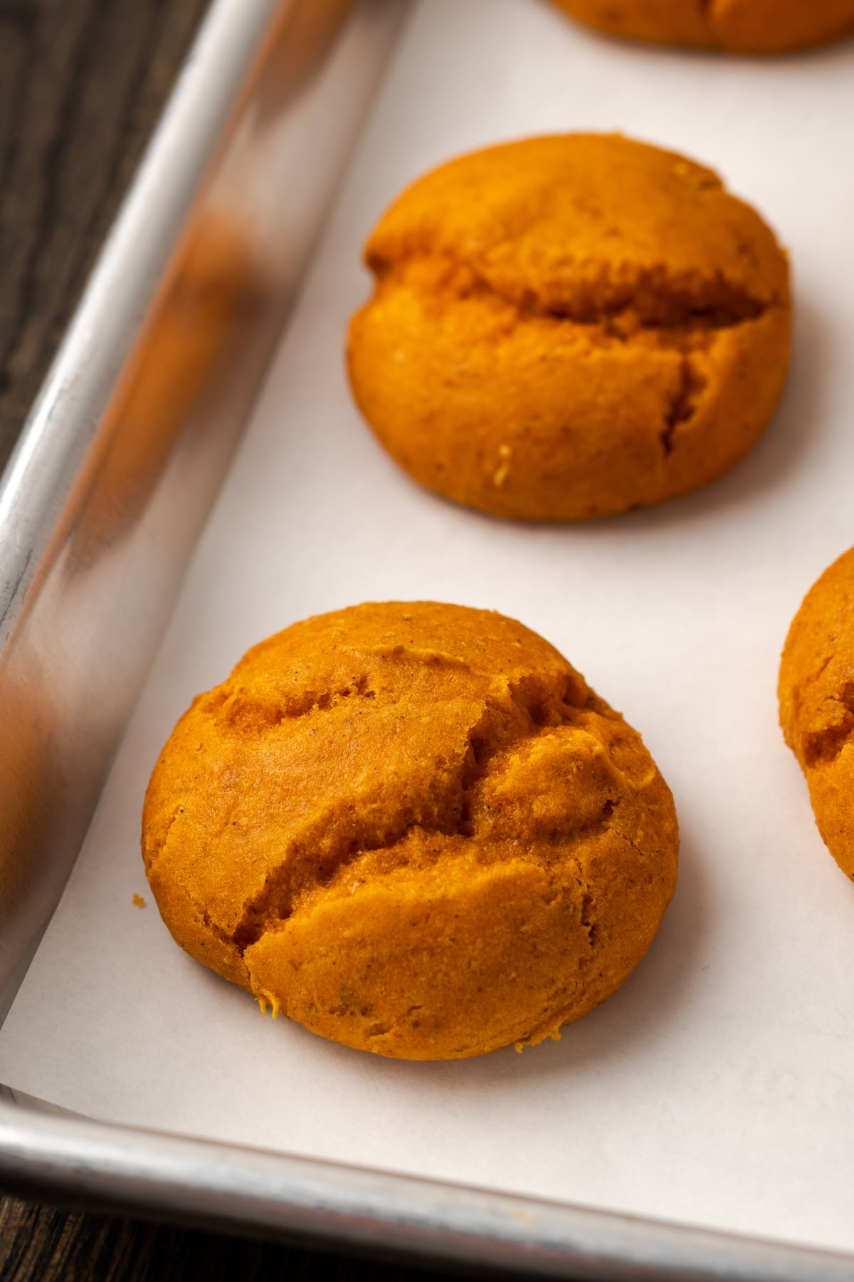 These soft and fluffy pumpkin cookies with cake mix are an easy fall dessert, made with only 2 ingredients and ready for the oven in minutes! Close up of baked cake mix pumpkin cookies on a metal baking sheet.