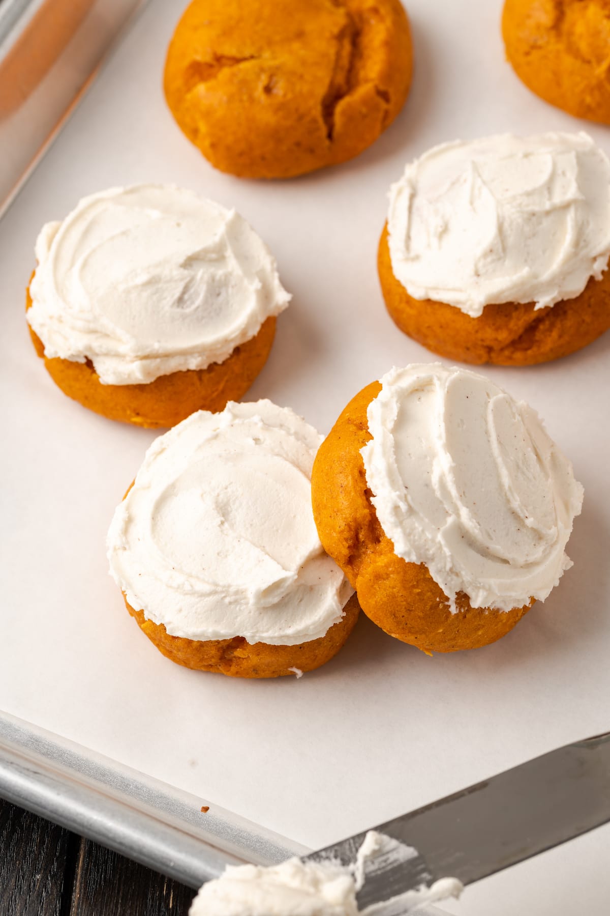 These soft and fluffy pumpkin cookies with cake mix are an easy fall dessert, made with only 2 ingredients and ready for the oven in minutes! Assorted frosted cake mix pumpkin cookies on a baking sheet.