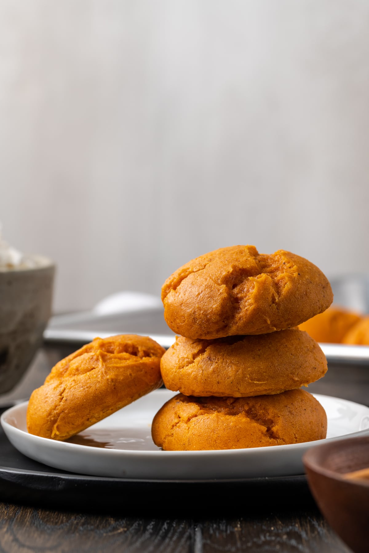 These soft and fluffy pumpkin cookies with cake mix are an easy fall dessert, made with only 2 ingredients and ready for the oven in minutes! Three cake mix pumpkin cookies stacked on a plate, with a fourth cookie leaning against the stack.