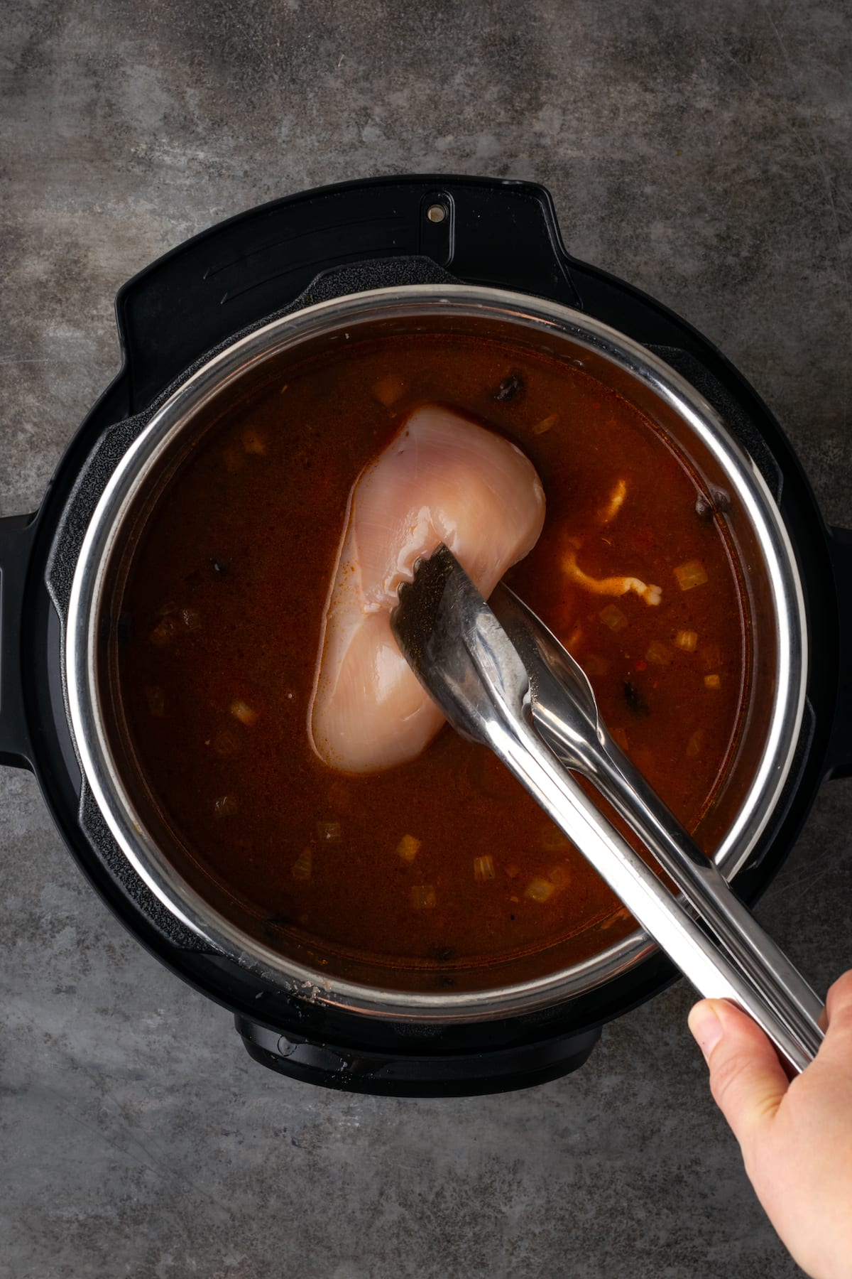 Smoky and flavorful Instant Pot chicken tortilla soup is a comforting one-pot meal that's easy to make any night of the week! Tongs are used to lower a raw chicken breast into tortilla soup in the Instant Pot.
