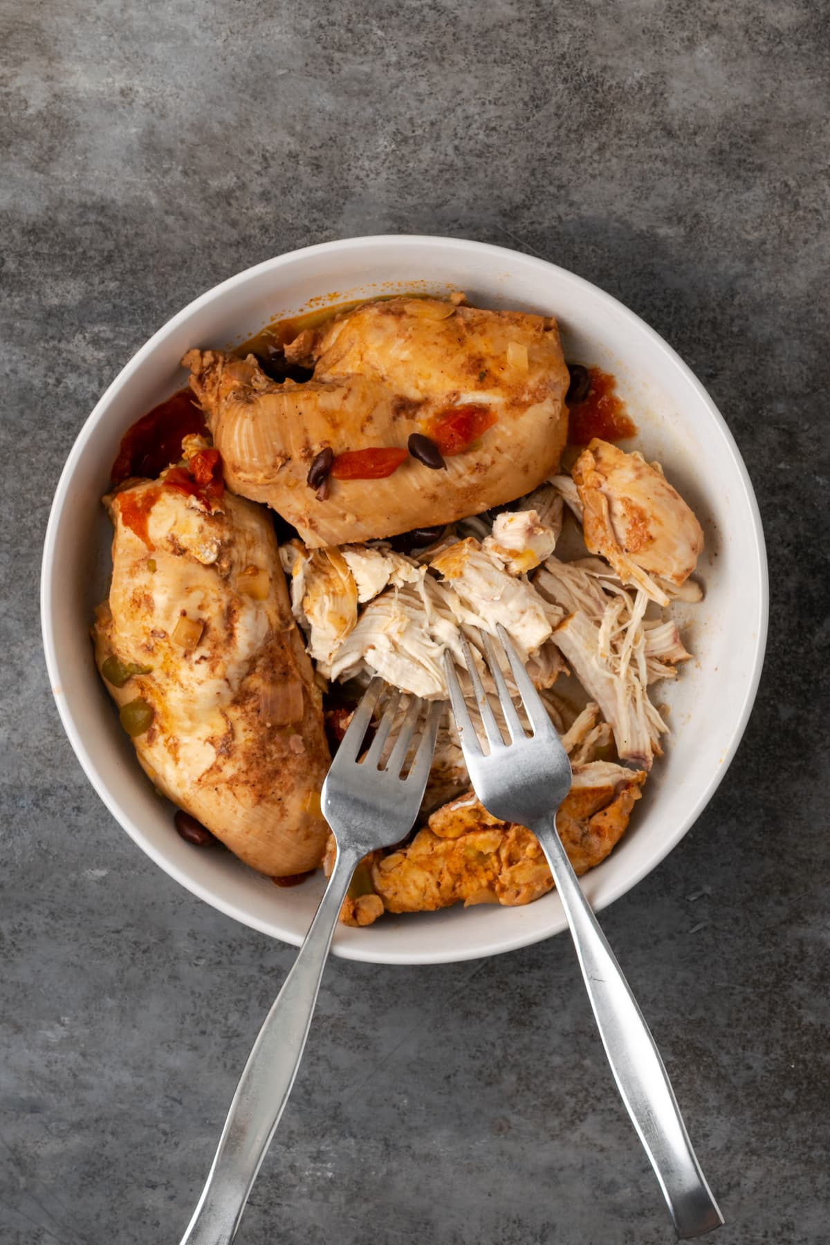 Smoky and flavorful Instant Pot chicken tortilla soup is a comforting one-pot meal that's easy to make any night of the week! Two forks with partially shredded chicken in a white bowl.