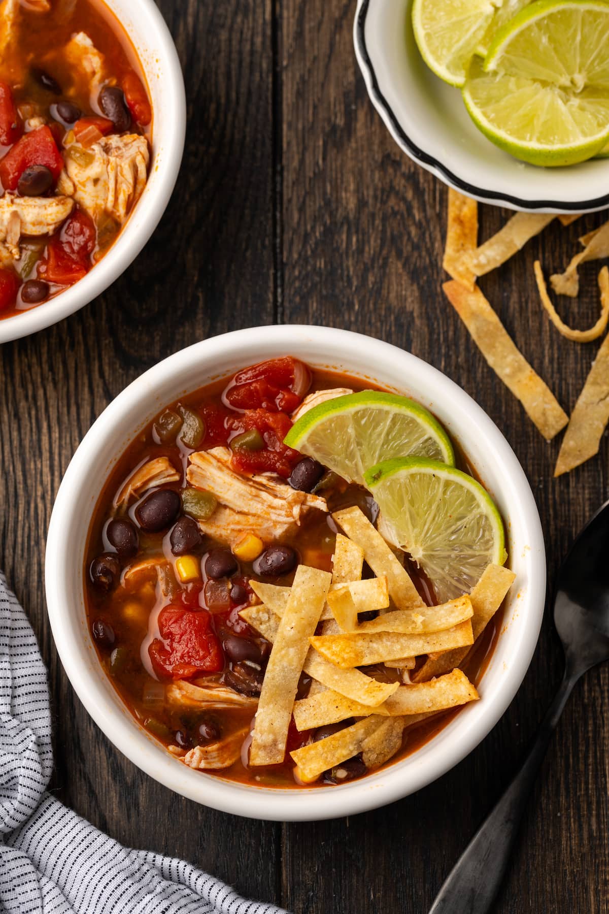 Smoky and flavorful Instant Pot chicken tortilla soup is a comforting one-pot meal that's easy to make any night of the week! Overhead view of a bowl of chicken tortilla soup garnished with lime wedges and crispy tortilla strips, next to bowls of more soup and lime wedges.