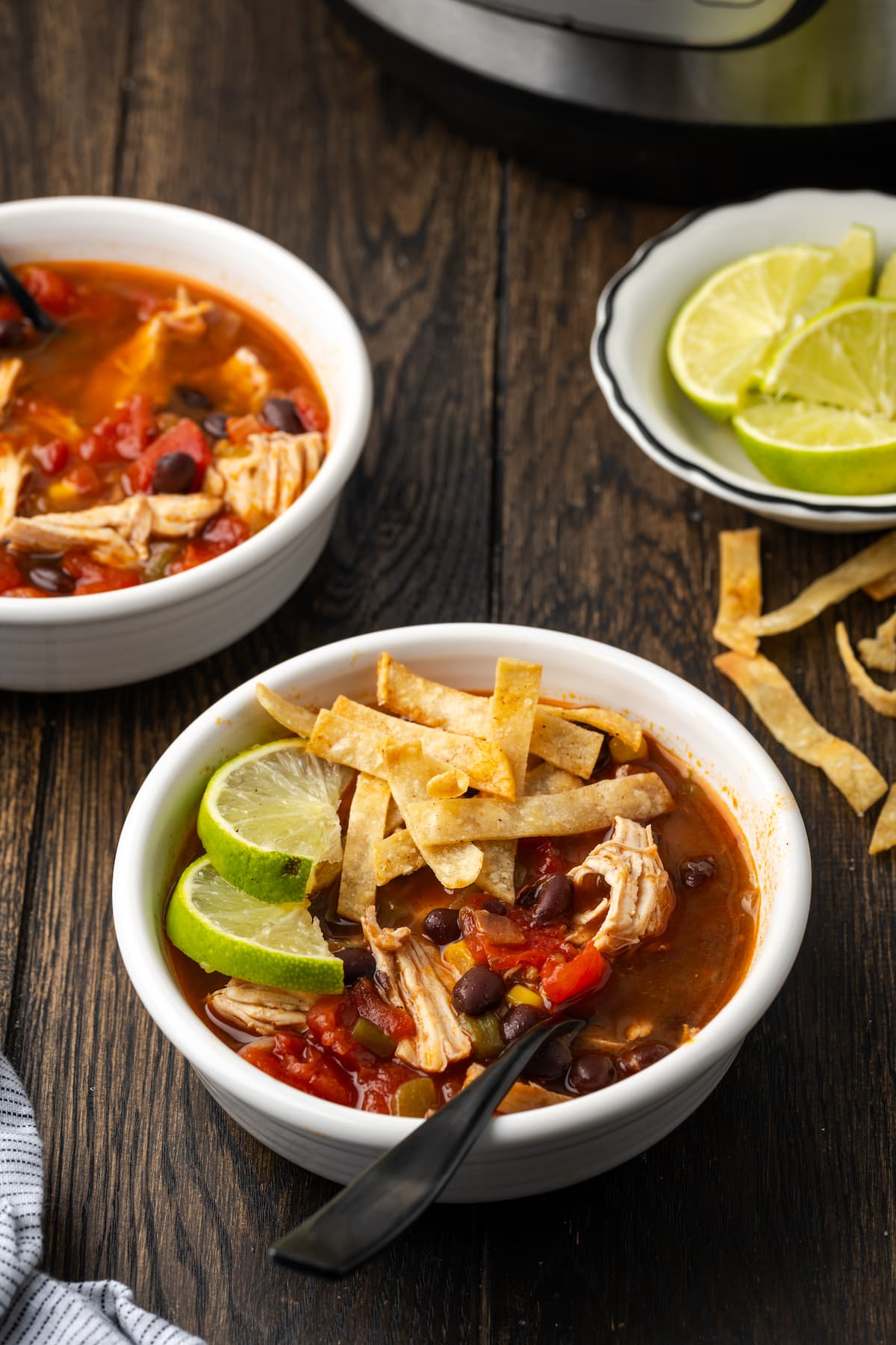 Smoky and flavorful Instant Pot chicken tortilla soup is a comforting one-pot meal that's easy to make any night of the week! A bowl of chicken tortilla soup garnished with lime wedges and crispy tortilla strips, with a bowl of lime wedges in the background.