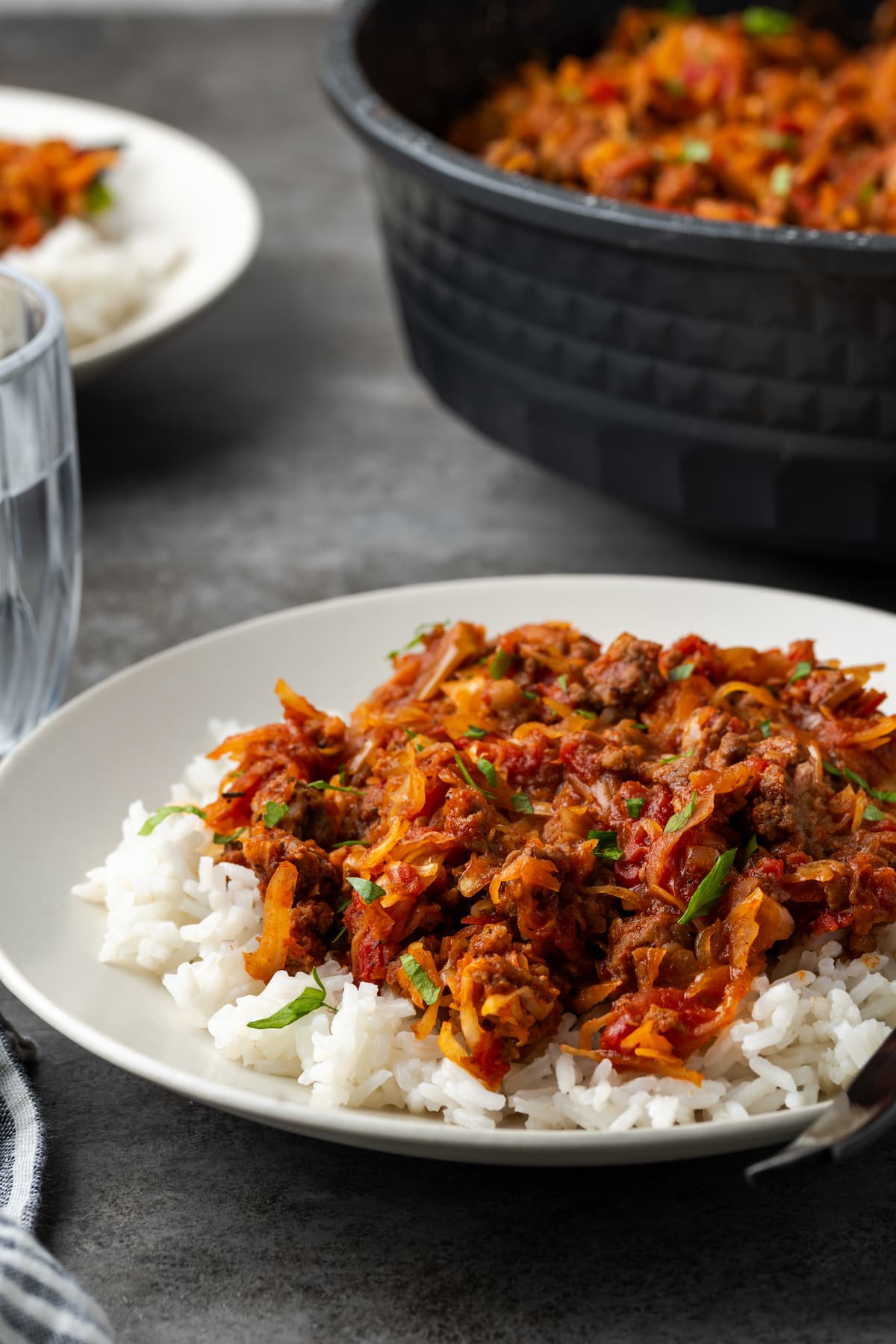 This easy unstuffed cabbage recipe is a savory one-pot meal made with juicy ground beef, pork, tangy fire-roasted tomatoes, and onions. Unstuffed cabbage served over rice on a white plate, with a large pot in the background.