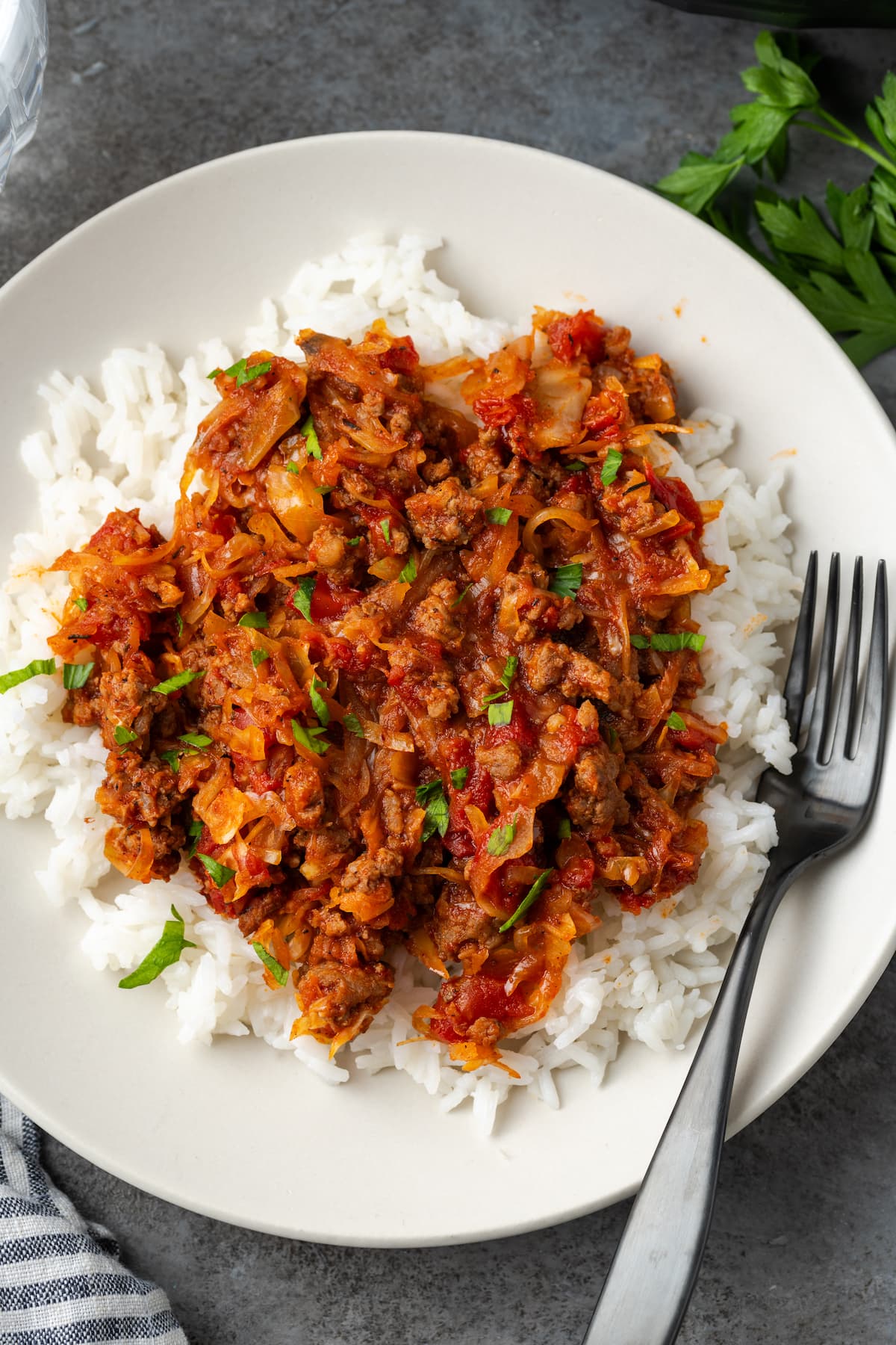 This easy unstuffed cabbage recipe is a savory one-pot meal made with juicy ground beef, pork, tangy fire-roasted tomatoes, and onions. Overhead view of unstuffed cabbage served over rice on a white plate next to a fork.