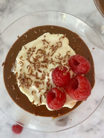 overhead view of chocolate mousse in a glass topped with cream and raspberries