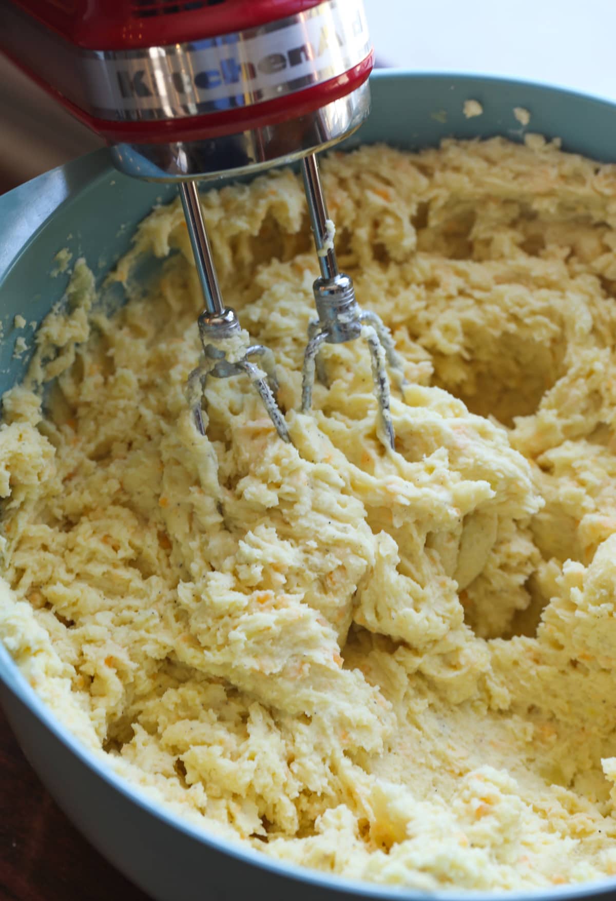 These Cheesy Baked Mashed Potatoes is the BEST mashed potato recipe ever! mashing potatoes in a blue mixing bowl with an electric hand mixer