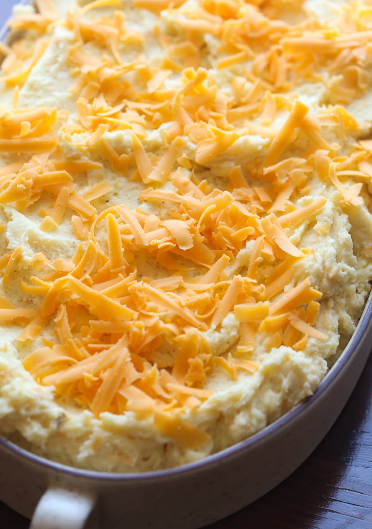 These Cheesy Baked Mashed Potatoes is the BEST mashed potato recipe ever! Mashed potatoes in a baking dish topped with grated cheese before going into the oven