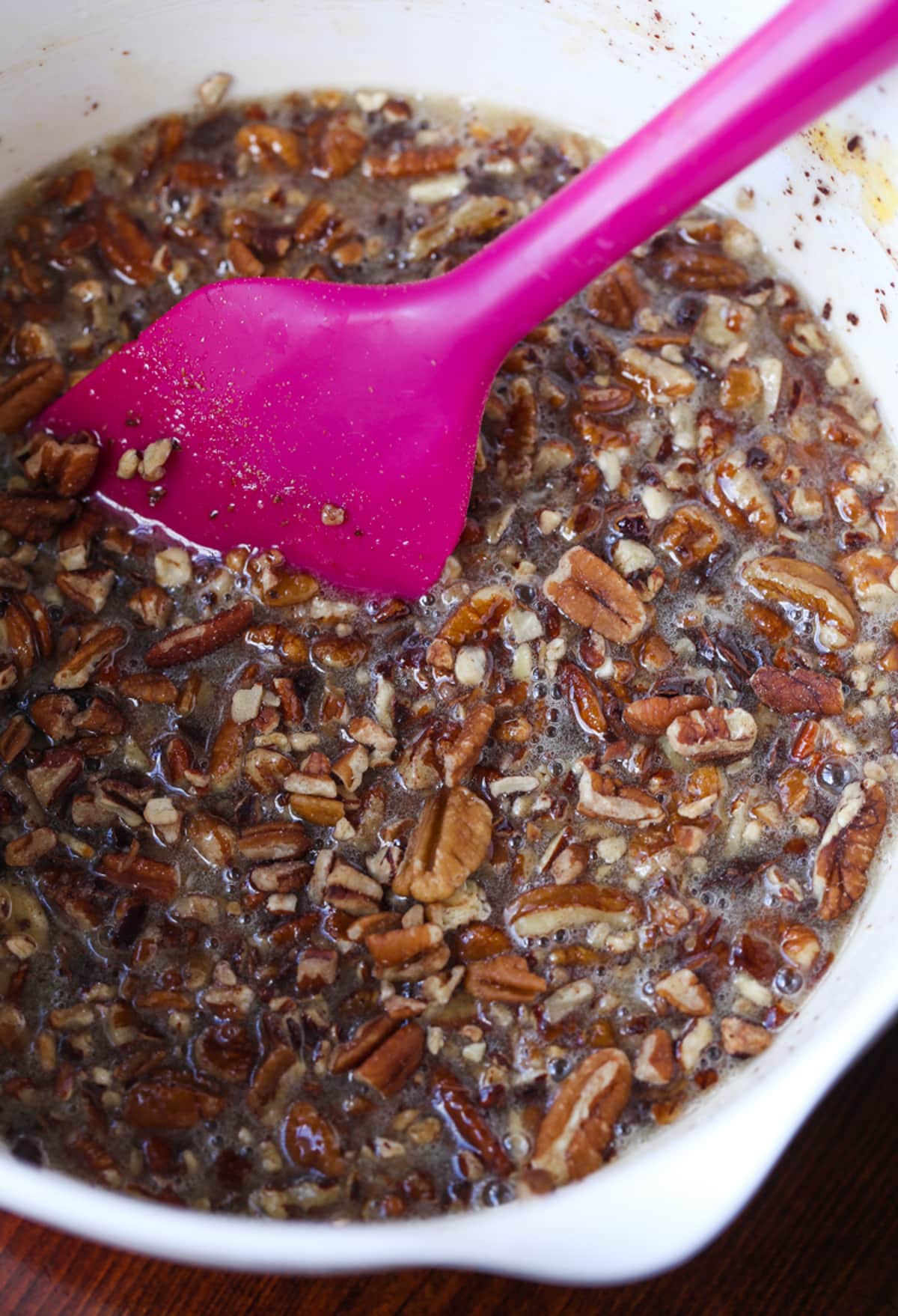 My EASY Chocolate Pecan Pie Recipe is a classic pecan pie recipe made even more delicious with melted chocolate, which turns the filling into a rich pudding-like texture loaded with pecans! Chocolate Pecan Pie filling in a mixing bowl with a pink rubber spatula
