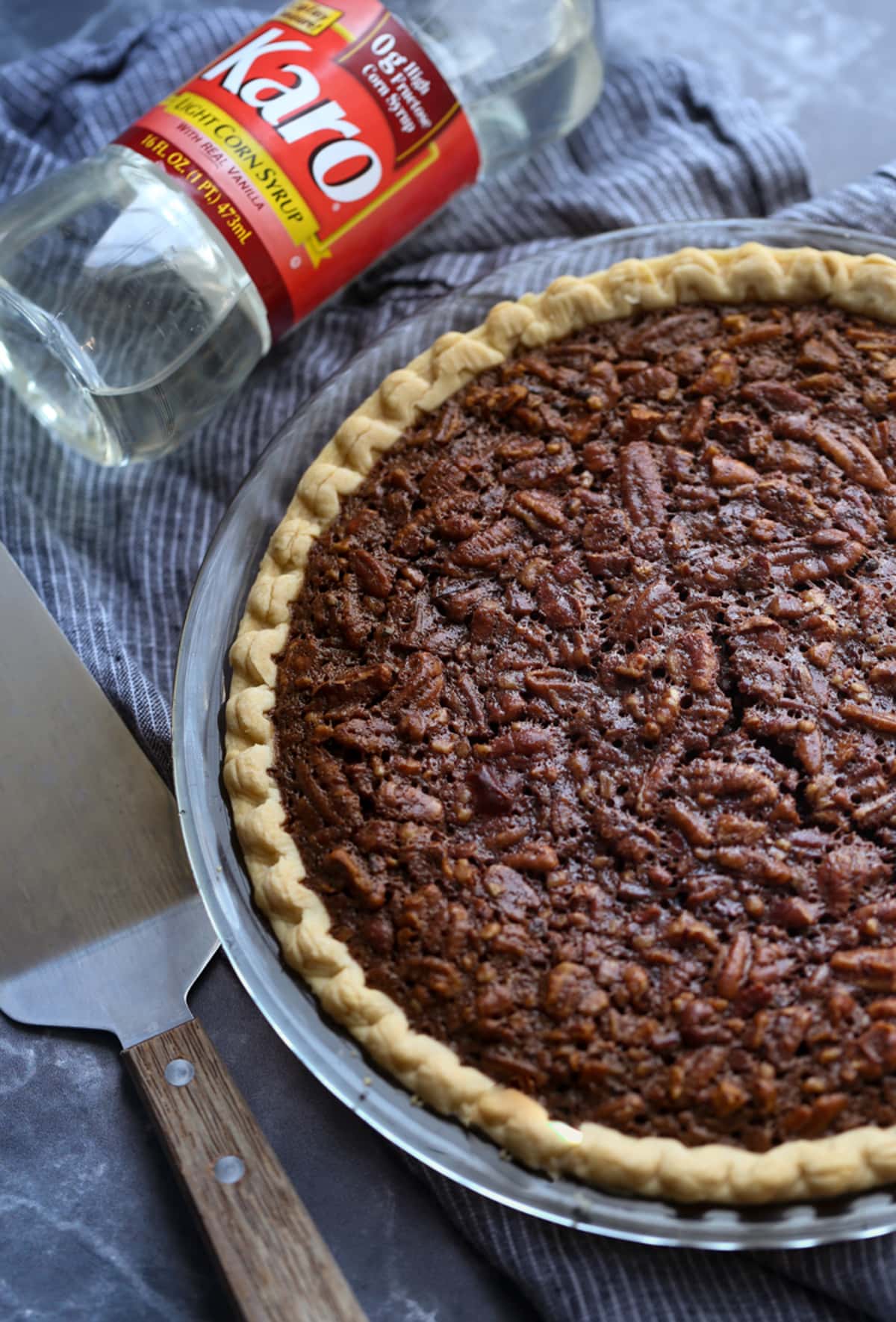 A baked chocolate pecan pie from above in a pie plate with a bottle of light corn syrup.