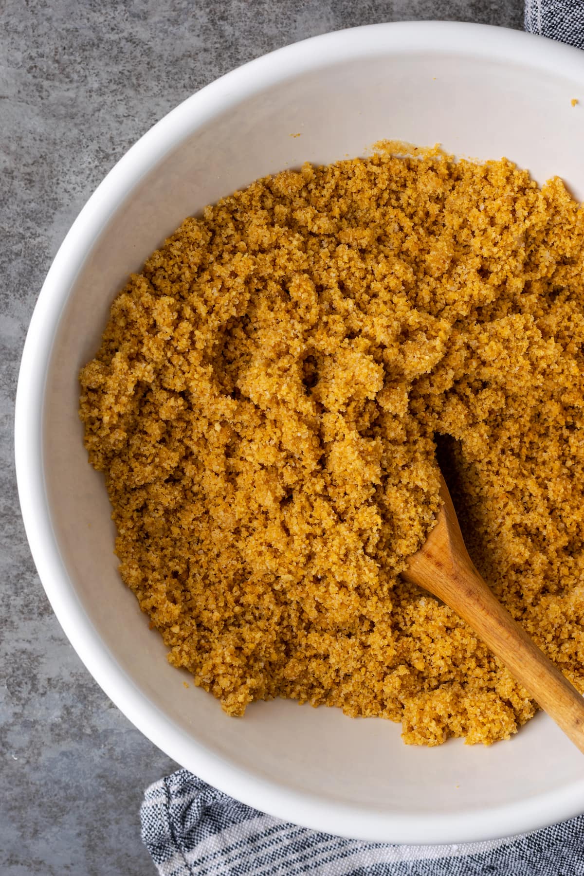 Creamy Butterfinger Pie is an easy dessert recipe that's loaded with Butterfinger candy bars! Treat yourself to this tasty peanut butter pie! Graham cracker crumbs combined with butter, salt, and sugar in a large white mixing bowl with a wooden spoon.
