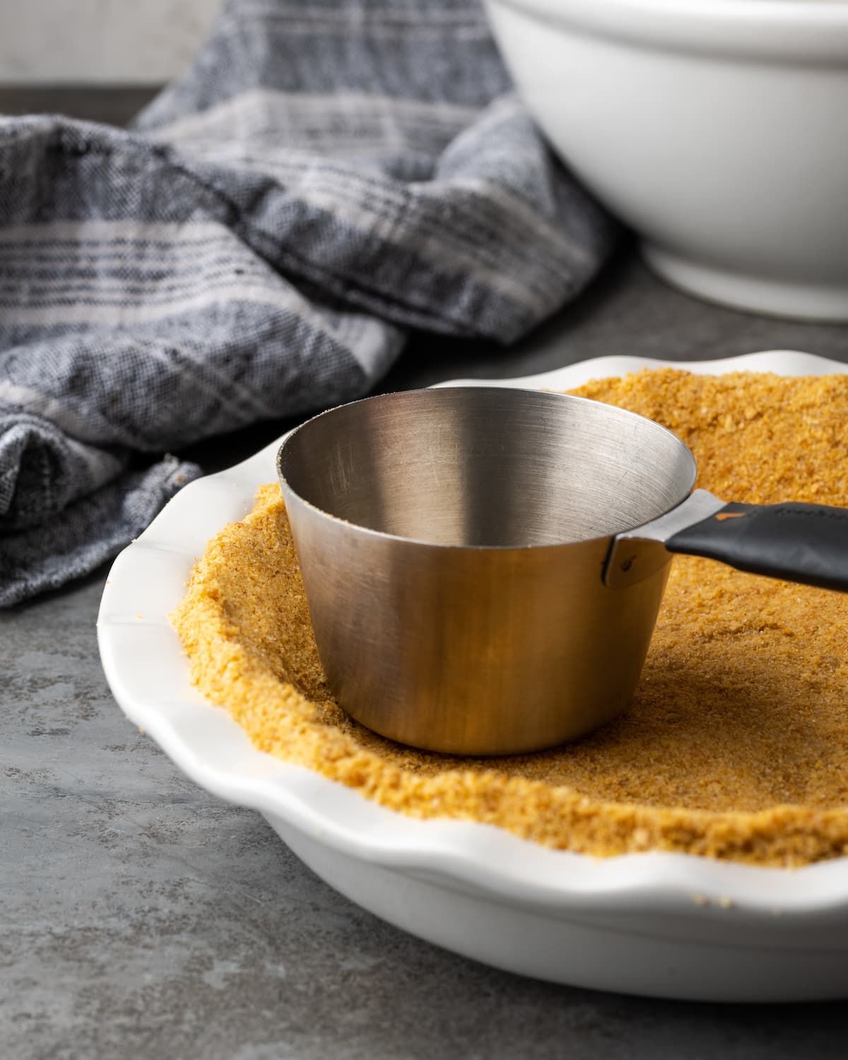 Creamy Butterfinger Pie is an easy dessert recipe that's loaded with Butterfinger candy bars! Treat yourself to this tasty peanut butter pie! A metal measuring cup is used to press the graham cracker crust into a white pie dish.
