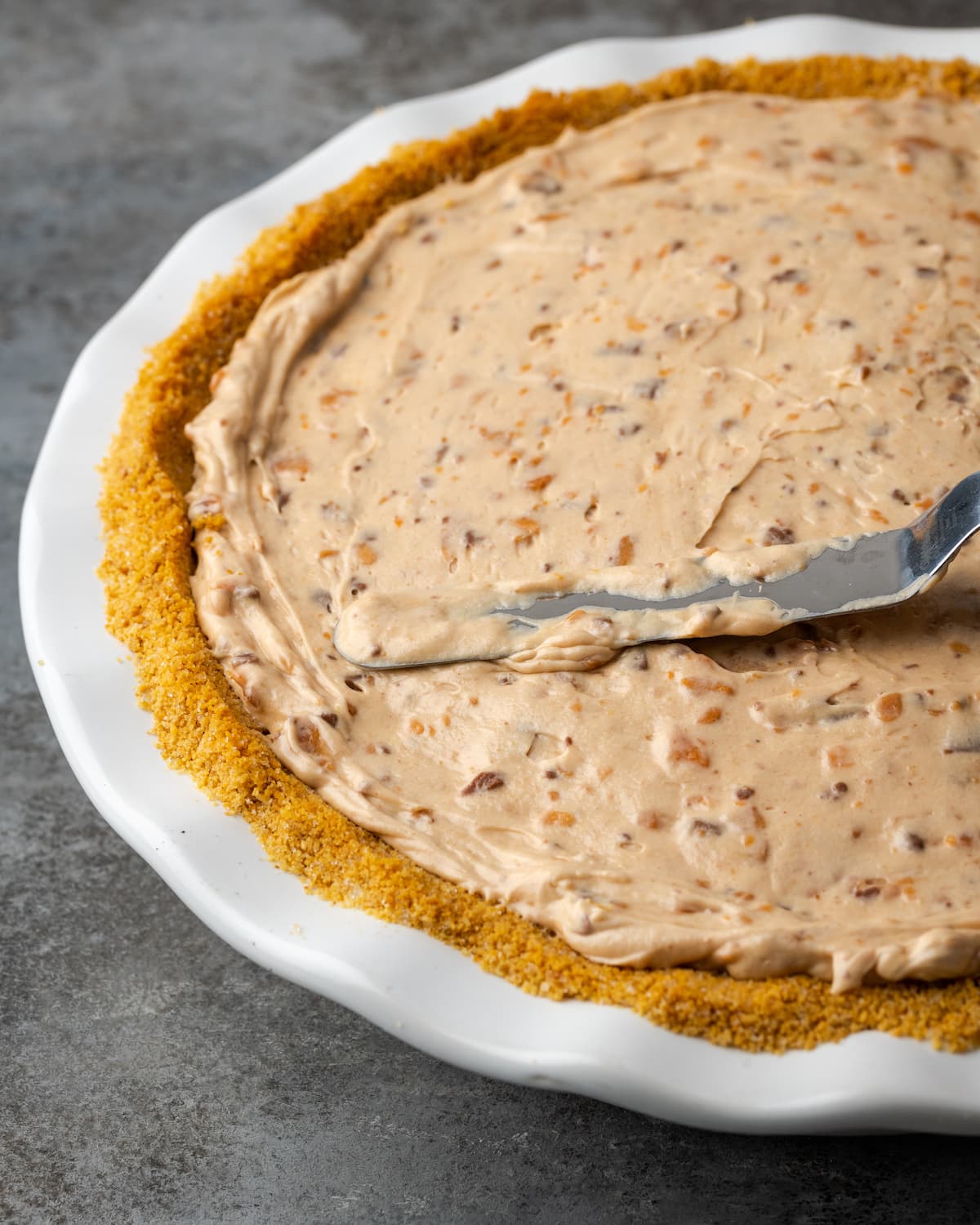 Creamy Butterfinger Pie is an easy dessert recipe that's loaded with Butterfinger candy bars! Treat yourself to this tasty peanut butter pie! Butterfinger pie filling is spread into a pie crust with an offset spatula.