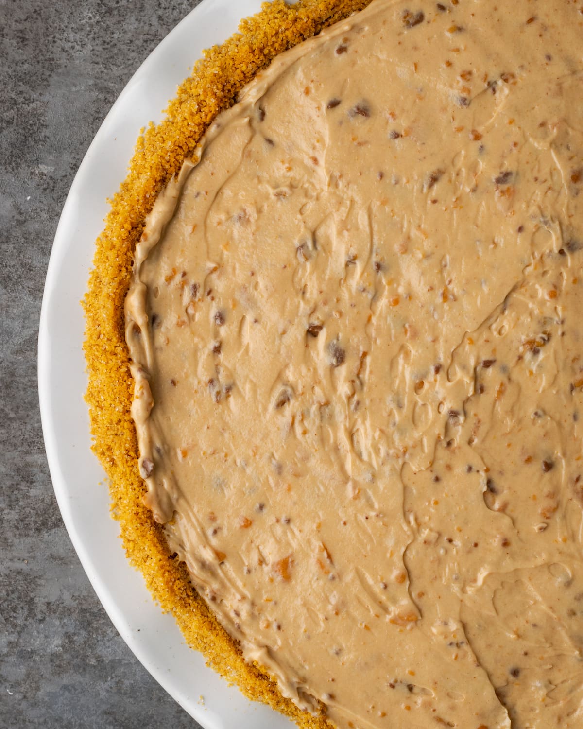 Creamy Butterfinger Pie is an easy dessert recipe that's loaded with Butterfinger candy bars! Treat yourself to this tasty peanut butter pie! Top view of Butterfinger pie asembled in a white pie dish.