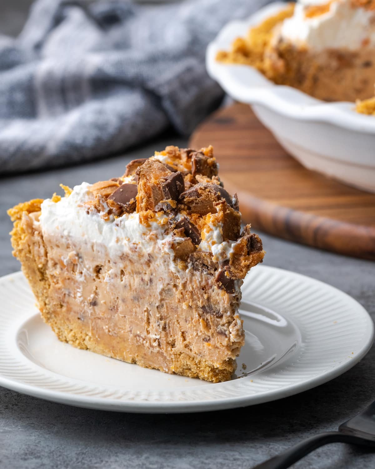 Creamy Butterfinger Pie is an easy dessert recipe that's loaded with Butterfinger candy bars! Treat yourself to this tasty peanut butter pie! A slice of Butterfinger pie on a white plate.
