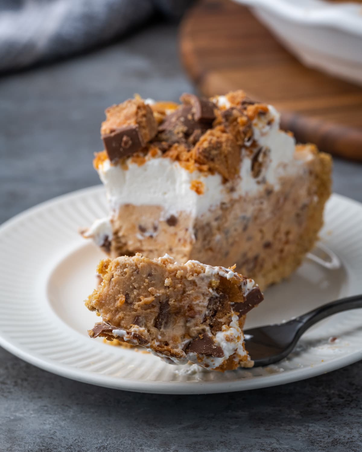 Creamy Butterfinger Pie is an easy dessert recipe that's loaded with Butterfinger candy bars! Treat yourself to this tasty peanut butter pie! A forkful of Butterfinger pie on a white plate next to a pie slice.
