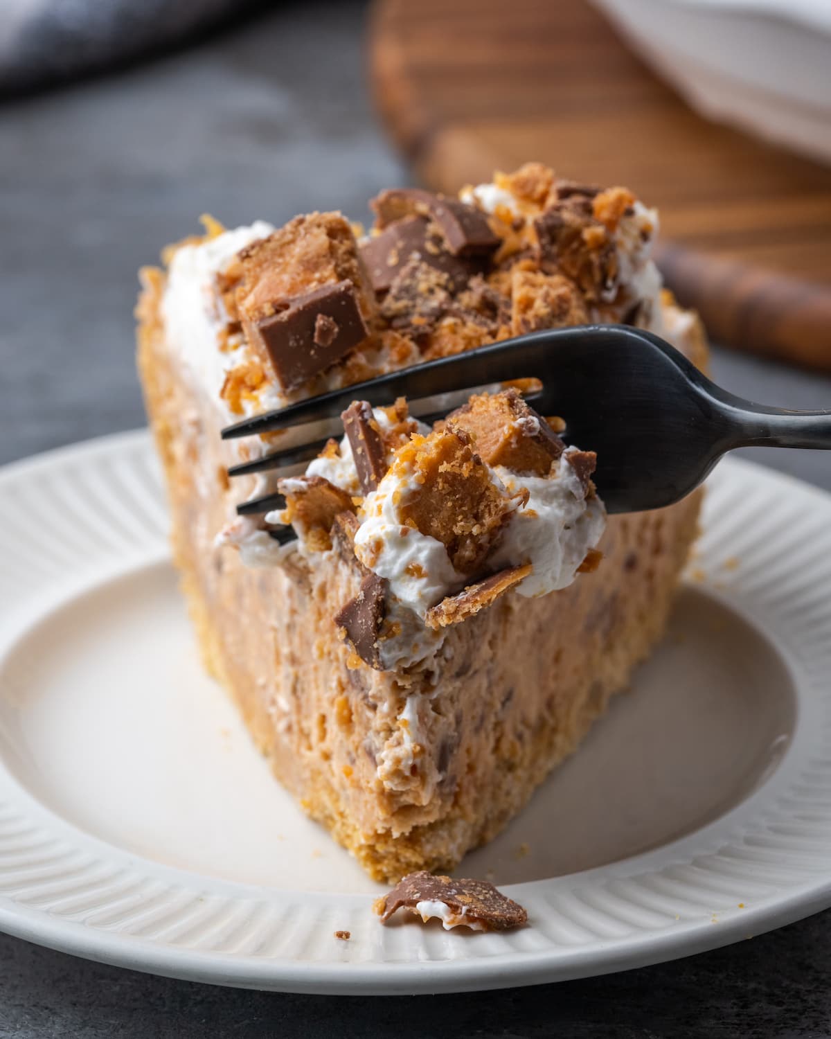 Creamy Butterfinger Pie is an easy dessert recipe that's loaded with Butterfinger candy bars! Treat yourself to this tasty peanut butter pie! A fork cuts into a slice of Butterfinger pie on a white plate.