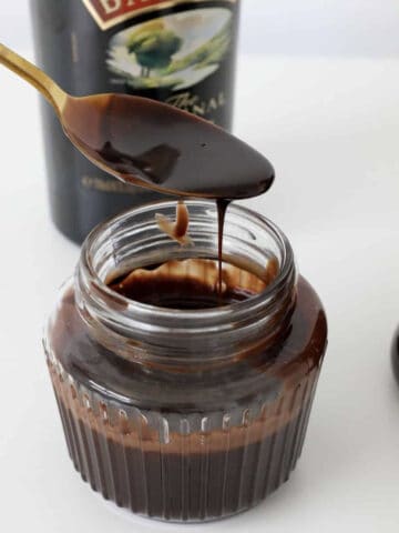 A gold spoon with chocolate sauce dripping from it.