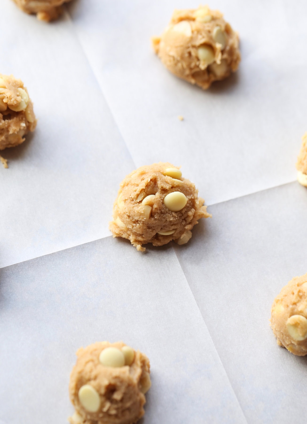 These white chocolate macadamia nut cookies are a classic. They have buttery, crisp edges with chewy centers loaded with creamy white chocolate and salty macadamia nuts. A scoop of white chocolate cookie dough on a parchment lined baking sheet