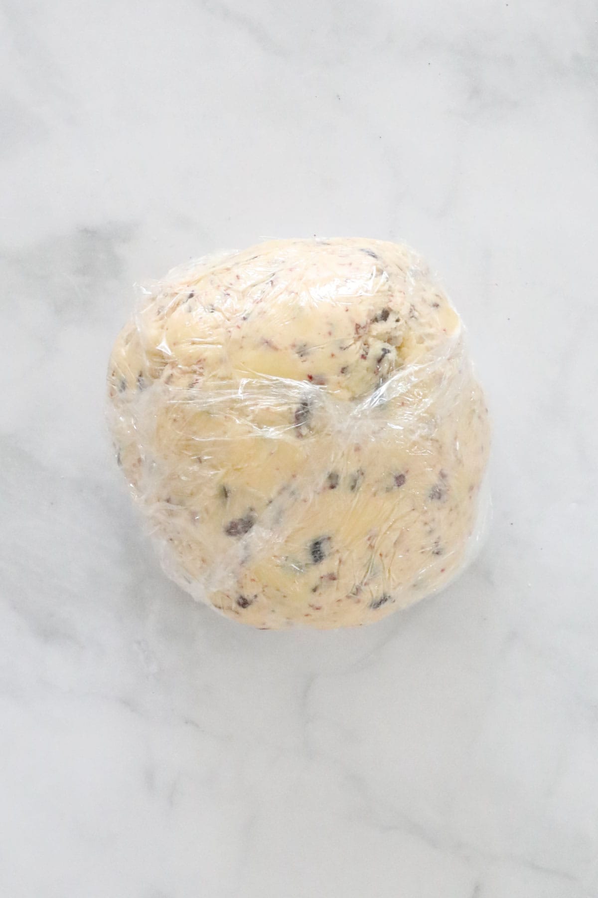 A ball of shortbread dough wrapped in plastic wrap.