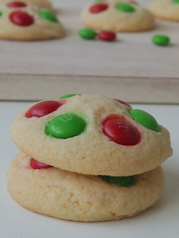 Two Christmas Biscuits made in a Thermomix stacked on top of each other and sitting in front of a wooden plate with more Christmas Biscuits on it.