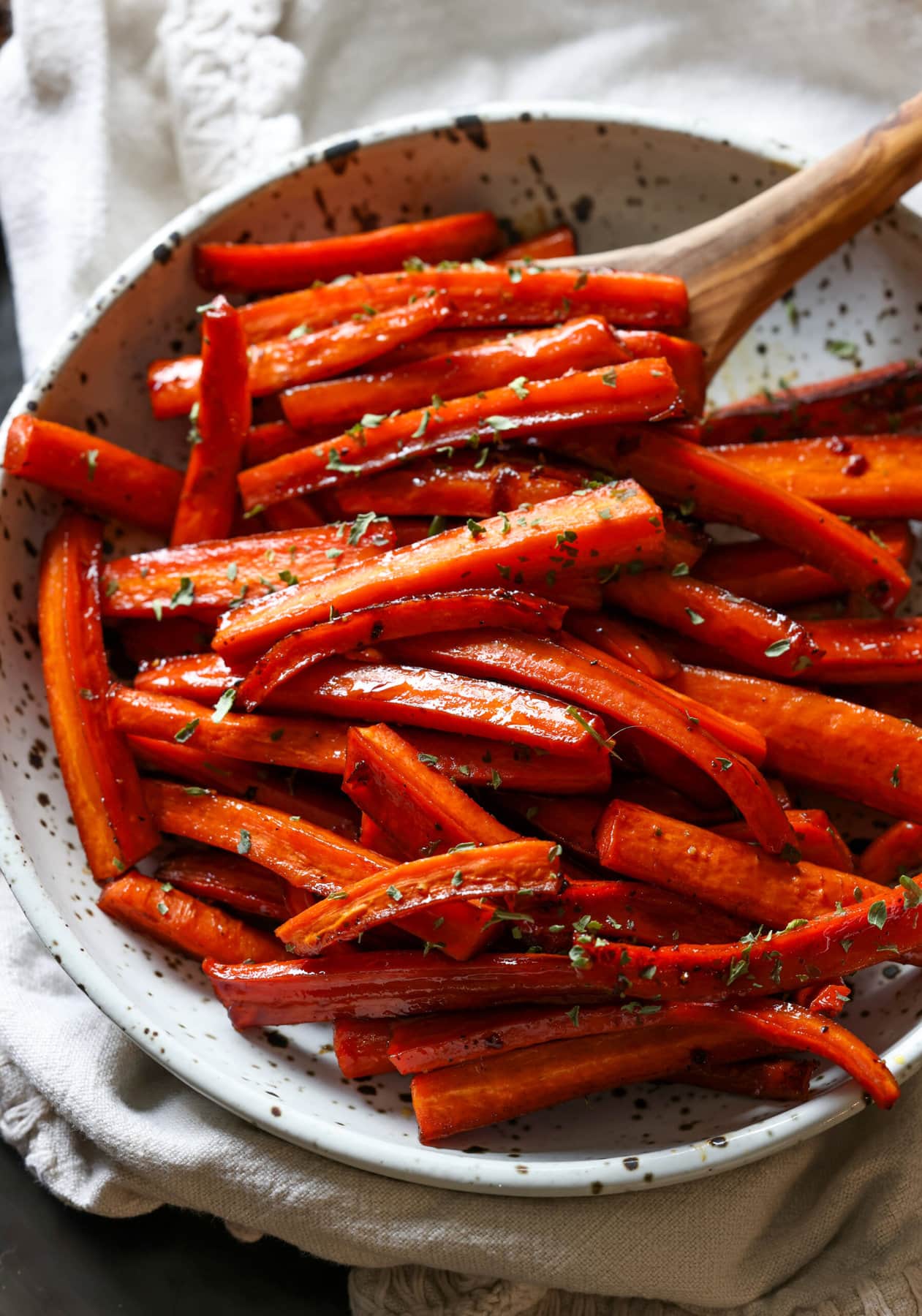 Roasted carrots in a serving bowl with a wooden serving spoon