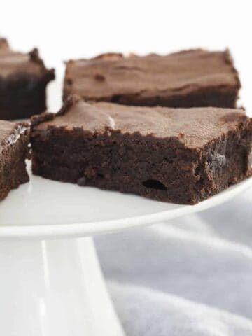 Slices of rich, chocolate brownies on a white cake stand.
