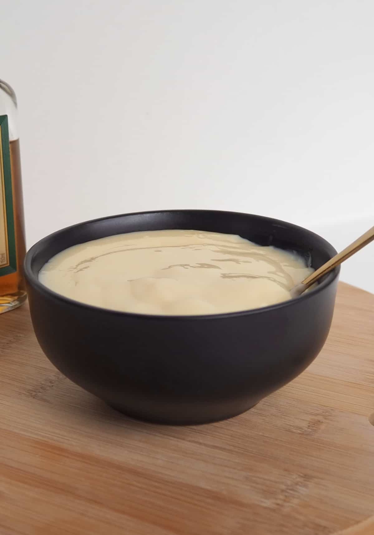 Brandy Custard in a black bowl sitting on a wooden board with a gold spoon sitting in it.